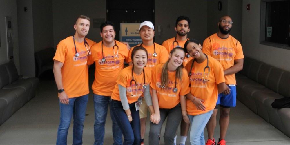 图为一群不同的学生穿着相同的橙色t恤，上面写着“特殊奥林匹克盛会”,在室内微笑着摆姿势合影